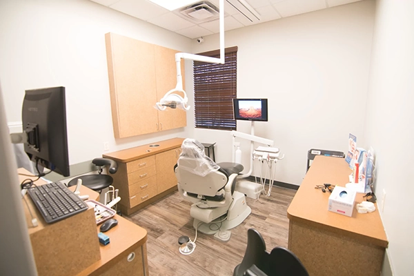 An exam room with an exam chair and blonde wooden cabinetry.