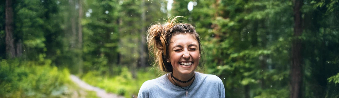 Dentist Avondale AZ Smiling Woman Outside A woman standing outside in a forest smiling.