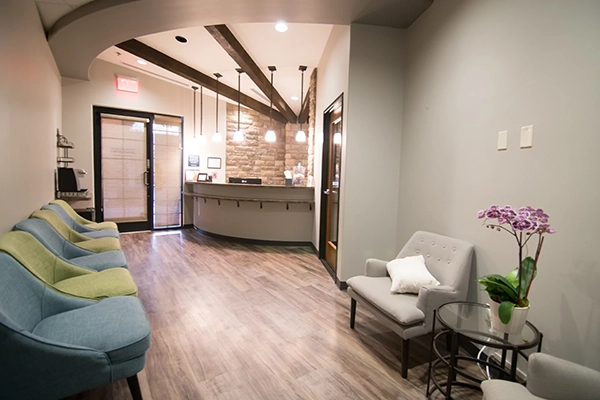 The waiting room of the clinic. The room has green and blue chairs with an orchid on an end table.